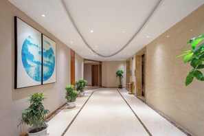 A corridor with a tiled floor, potted plants, and framed artwork on the walls. - Fusion International Hotel (Yizhang)