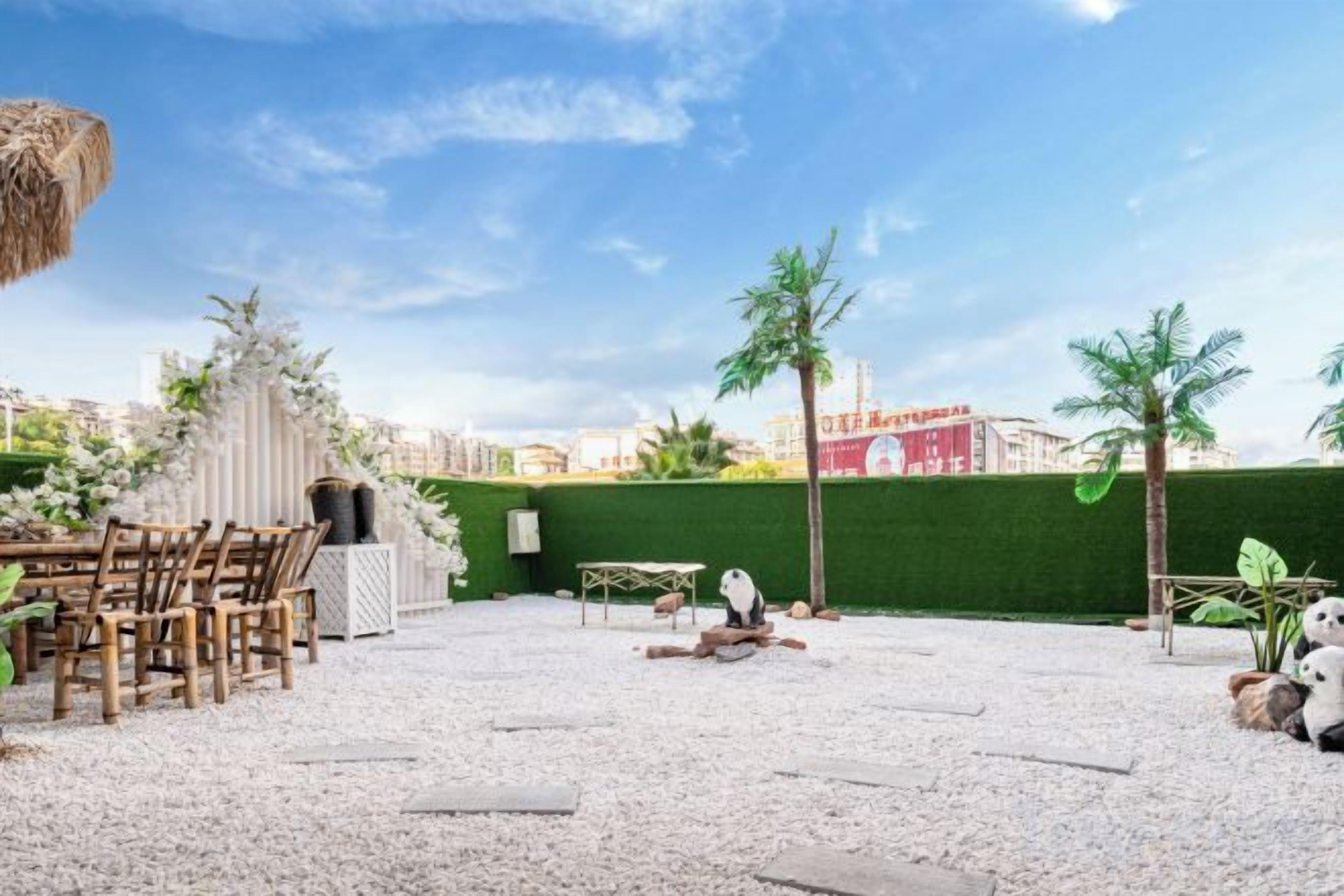 Un área de estar al aire libre con una mesa, sillas, techo de paja y un seto verde.