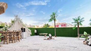Un área de estar al aire libre con una mesa, sillas, techo de paja y un seto verde.
