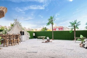 An outdoor seating area with a table and chairs, a thatched roof, and a green hedge. - Fusion International Hotel (Yizhang)