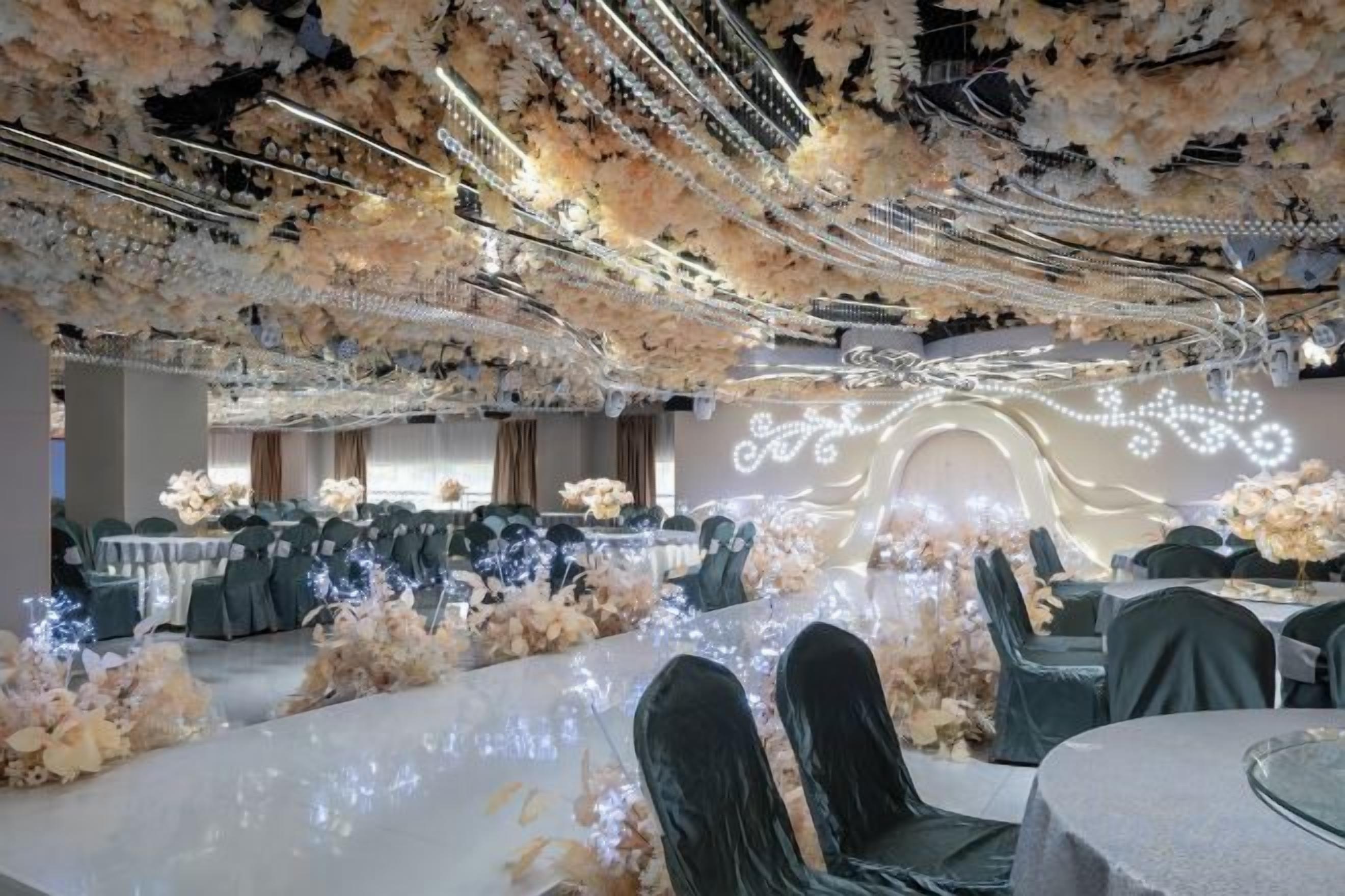 Une salle de banquet où les tables sont dressées pour des événements, décorées de compositions florales et recouvertes de tissu blanc.