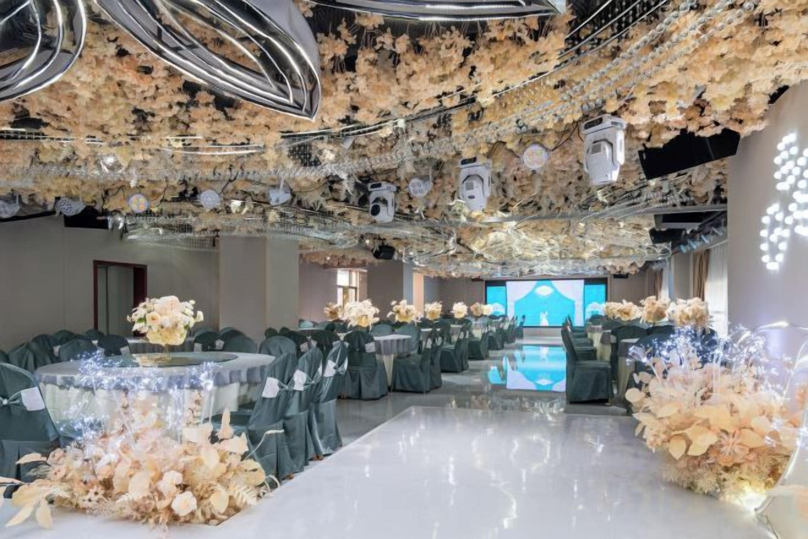 Un salón de banquetes con mesas dispuestas para eventos, un escenario al fondo y un techo decorado con motivos florales.