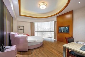 Una habitación de hotel moderna con una cama redonda, una silla de masaje, una mesa de comedor y un ventanal con vistas.