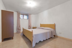A bedroom with a wooden bed, a nightstand, a window with curtains, and a door.