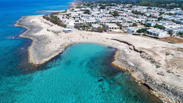 An aerial view of a coastal town with clear turquoise waters, sandy beaches, and a dense cluster of white buildings with blue accents. - 2815 Villetta la Siepe - Appartamento B by Barbarhouse (Taviano)