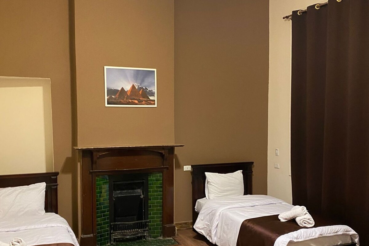 A hotel room with two beds, a fireplace, and a painting of pyramids.