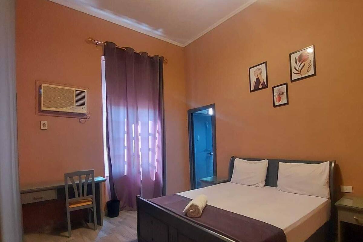 A bedroom with a bed, a desk, a chair, and a door.