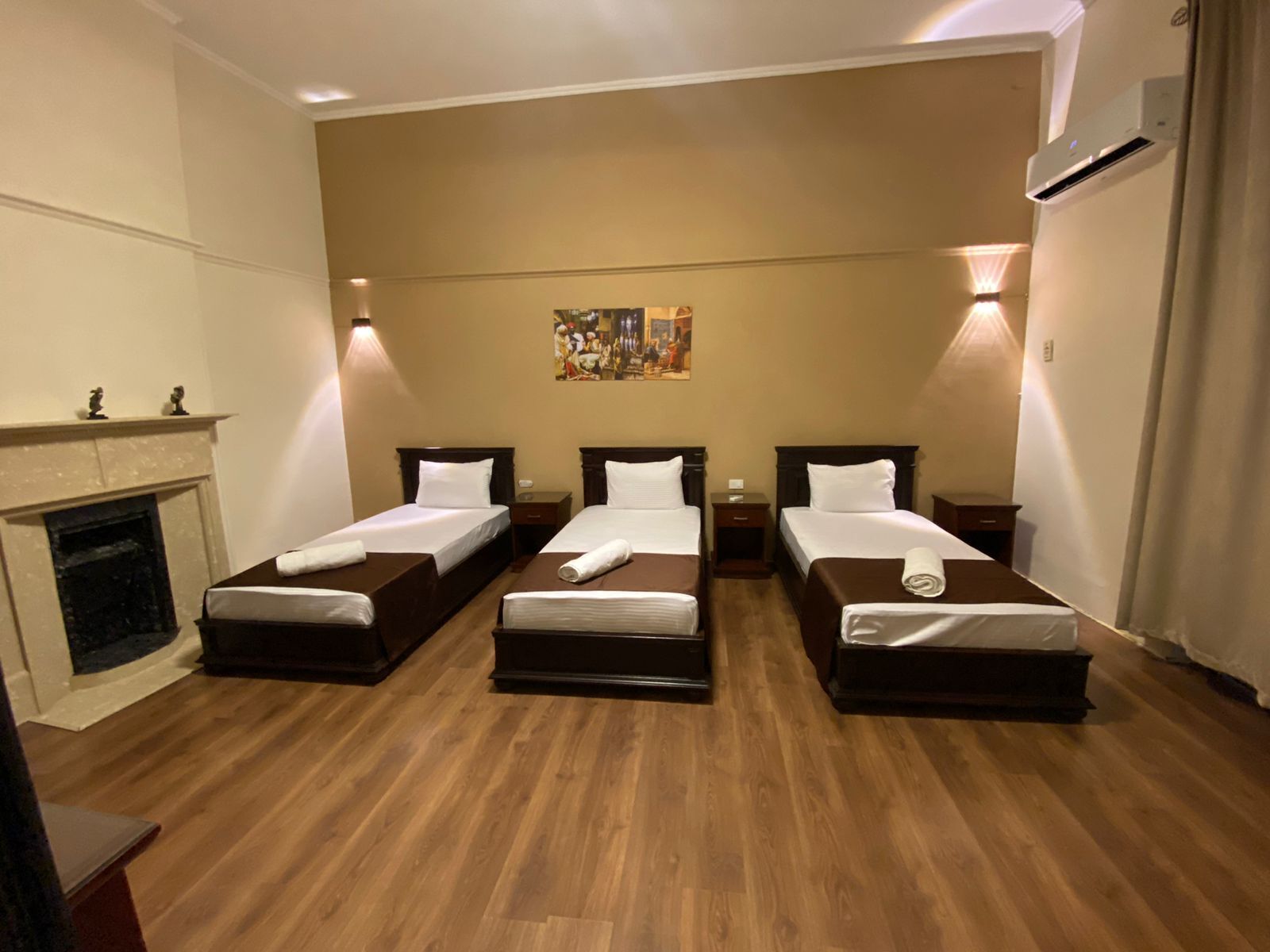A hotel room with three single beds, a fireplace, and a painting on the wall.