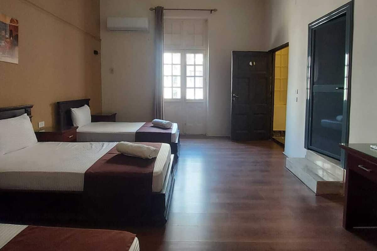 A hotel room with two beds, a large window, a door leading to a balcony, and a sliding glass door.