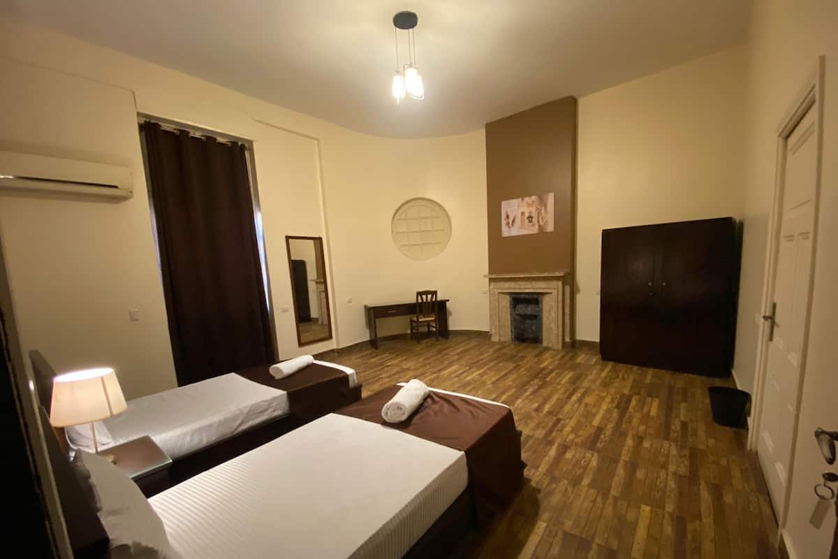 A hotel room with two beds, a desk, a chair, a fireplace, and a television.