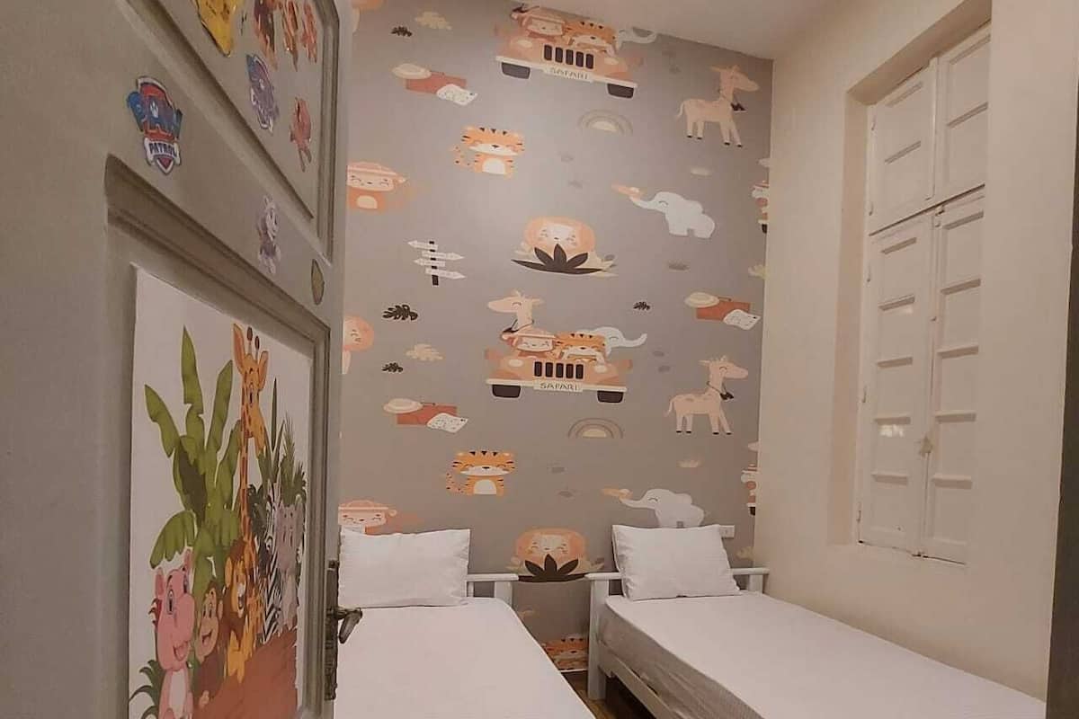 A children's room with two beds, a wall with safari-themed decals, and a door with a small window.