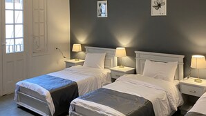Quarto de hotel com duas camas, uma janela grande e uma parede escura.