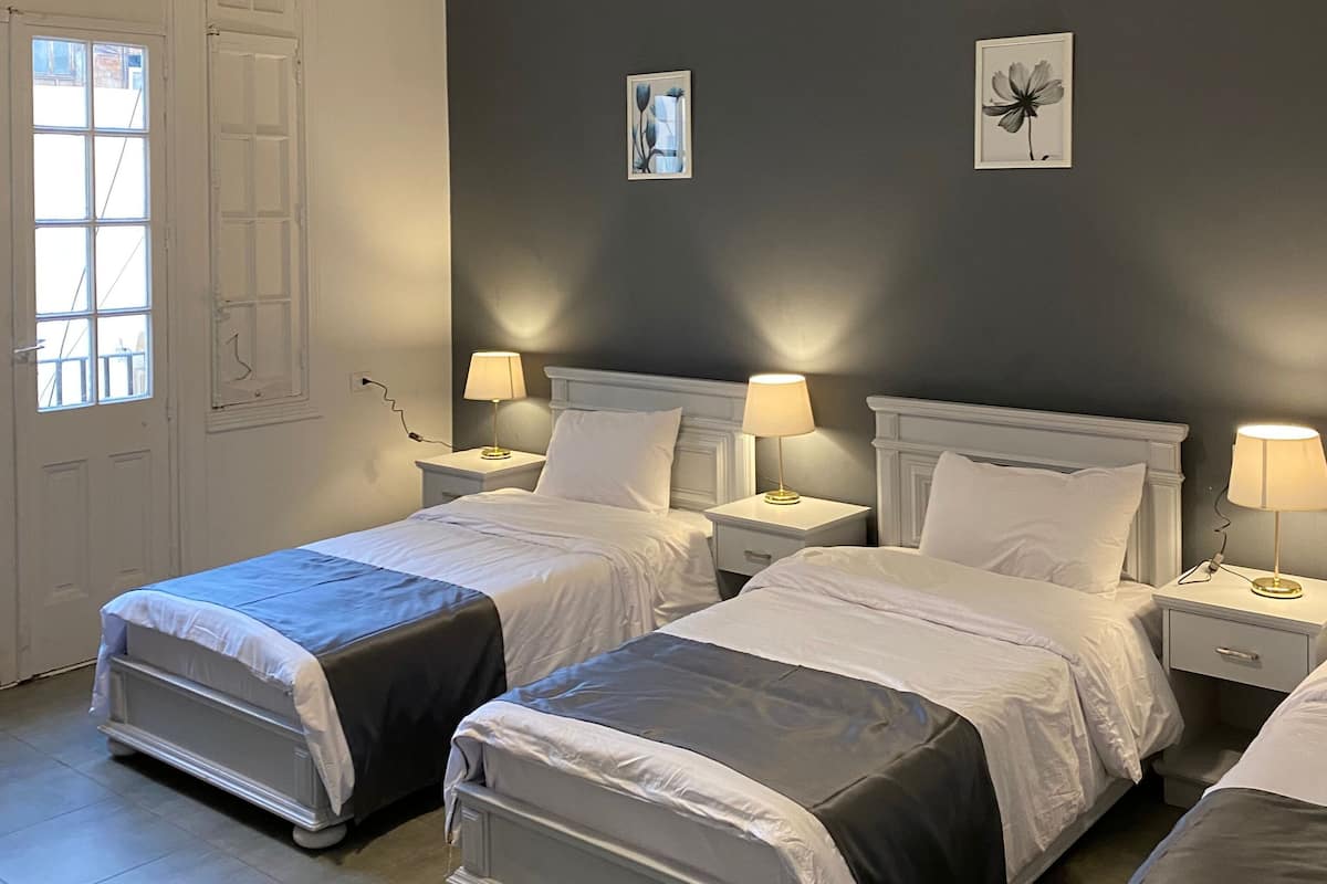 A hotel room with two beds, a large window, and a dark wall.
