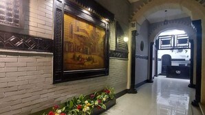 Um corredor com piso de azulejos, um quadro na parede e um vaso de flores.