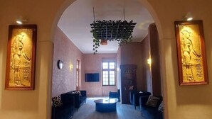 Um hall amplo com piso de mármore, área de estar central com sofás, mesa de centro e uma grande porta em arco.