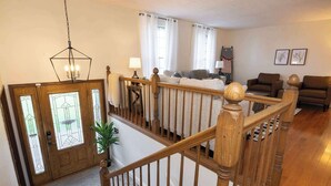 Eine Treppe mit Holzspindeln führt zu einem Wohnzimmer mit Sofa und braunem Ledersessel.