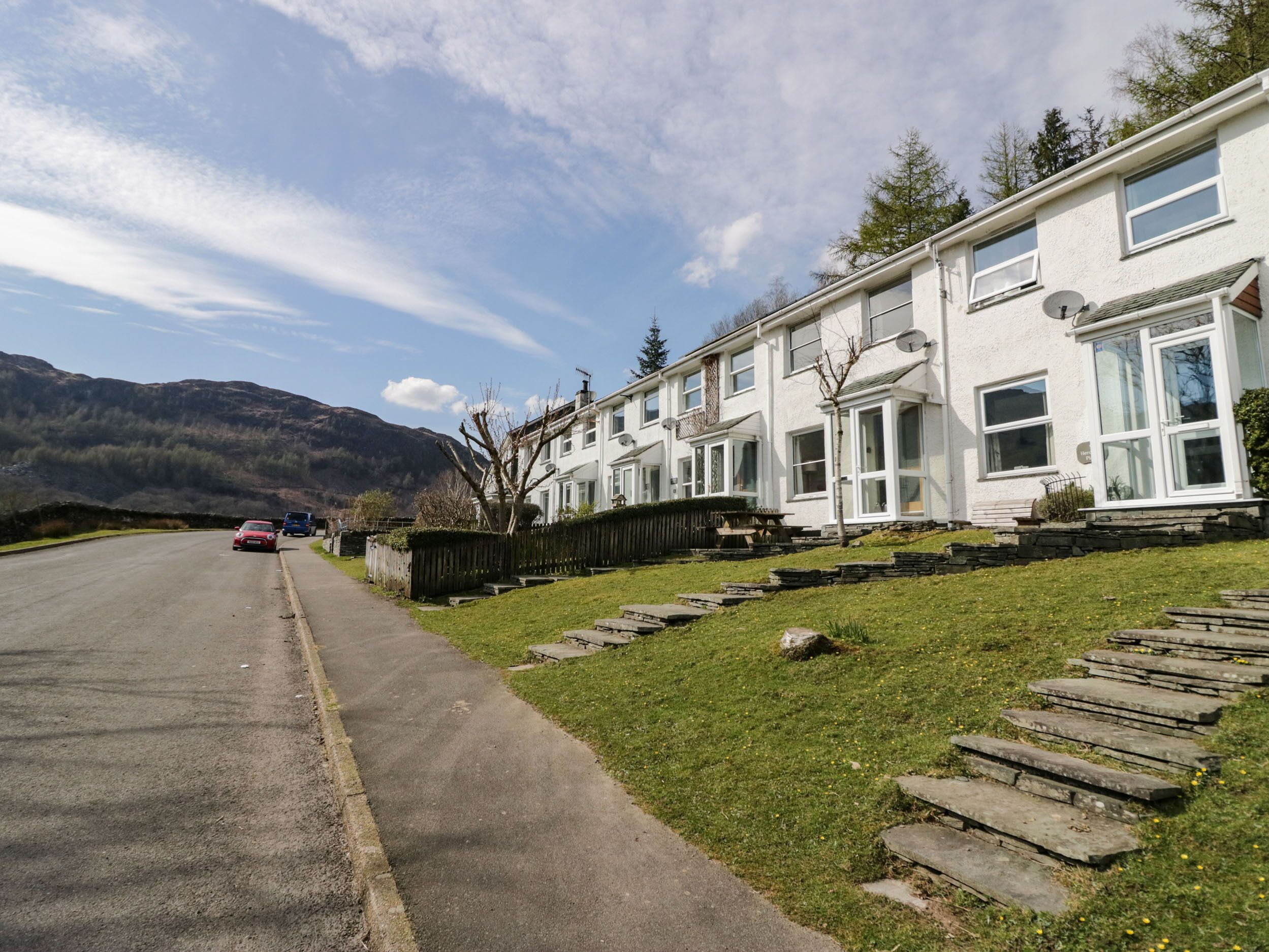 A row of white houses with large windows and satellite dishes, a paved road, and a grassy area with steps leading up to the houses.