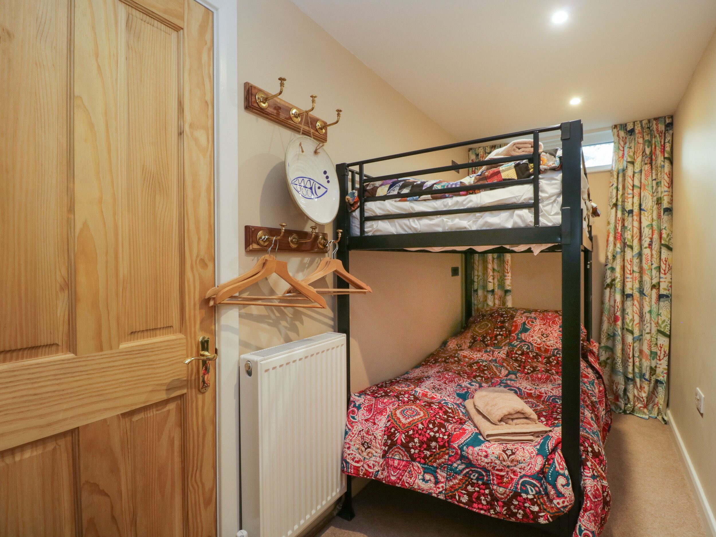 A small, compact room with a bunk bed, a wooden wardrobe, a radiator, and a wall-mounted shelf with a decorative plate.
