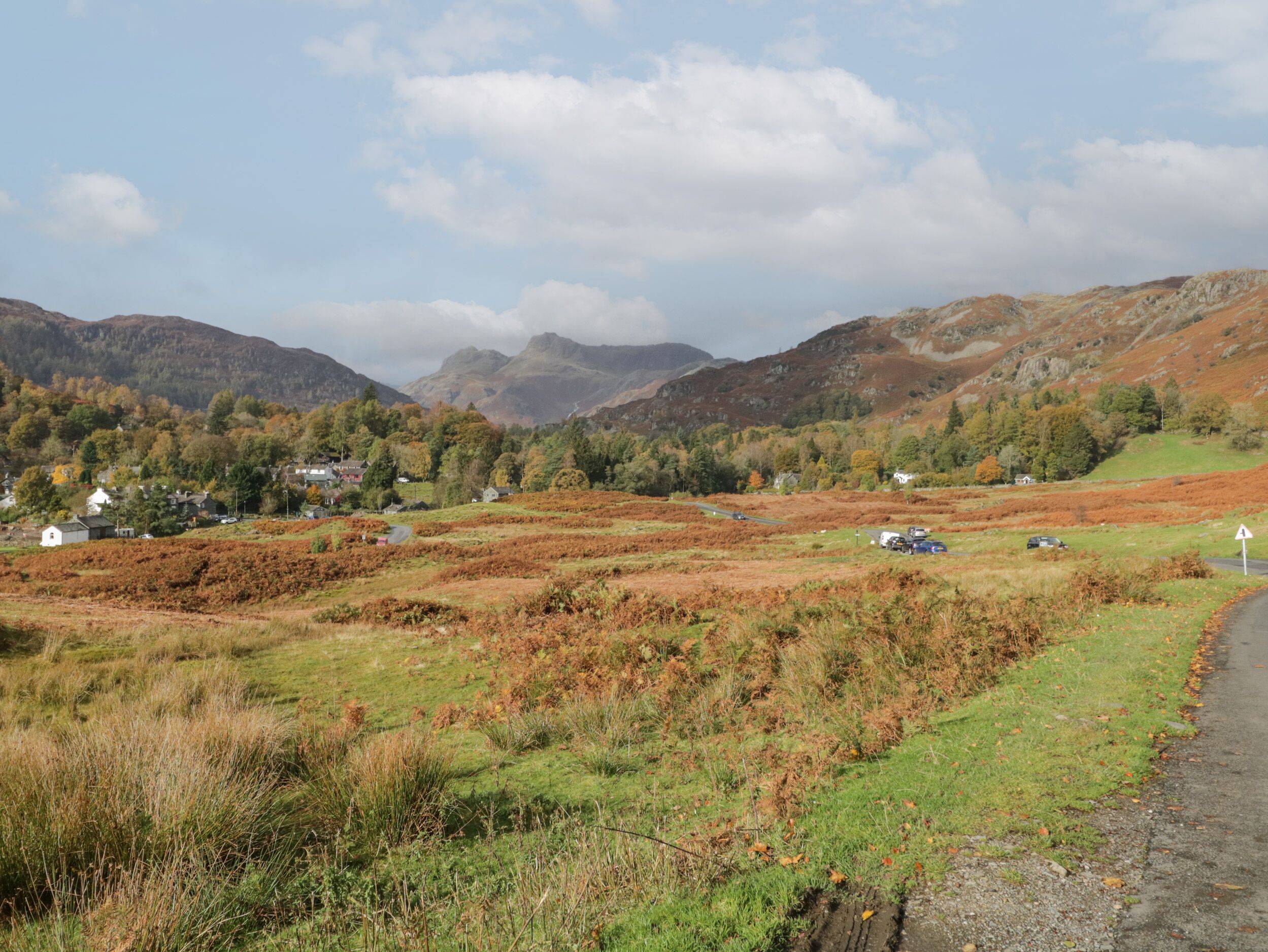 A rural landscape with rolling hills, a small village, and a road.