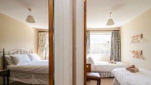 Habitación de hotel con dos camas, un armario de madera, un banco y una ventana con cortinas.