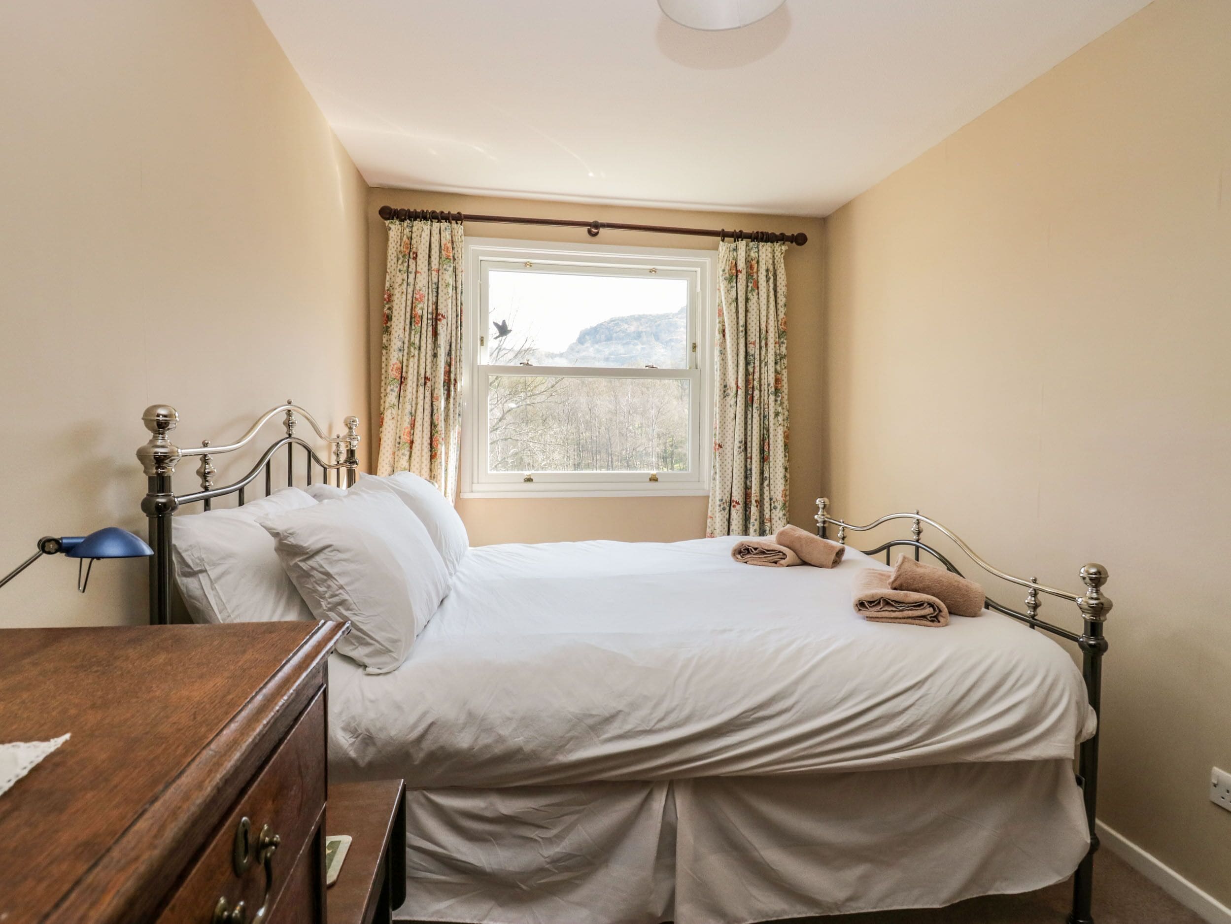 A bedroom with a bed, a wooden dresser, a window with curtains, and a view of the outdoors.
