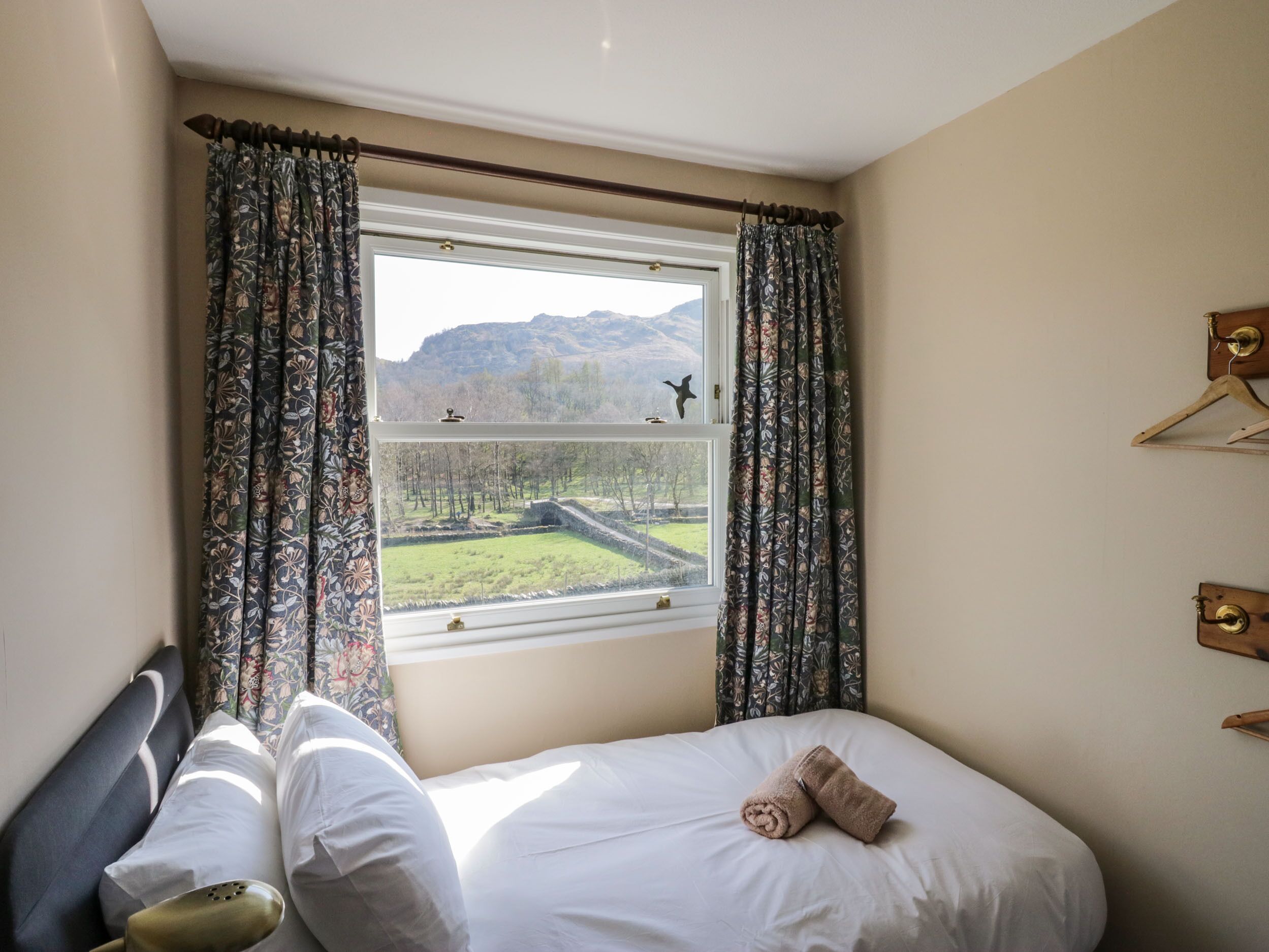 A bedroom with a bed, a window with curtains, and a view of a landscape.