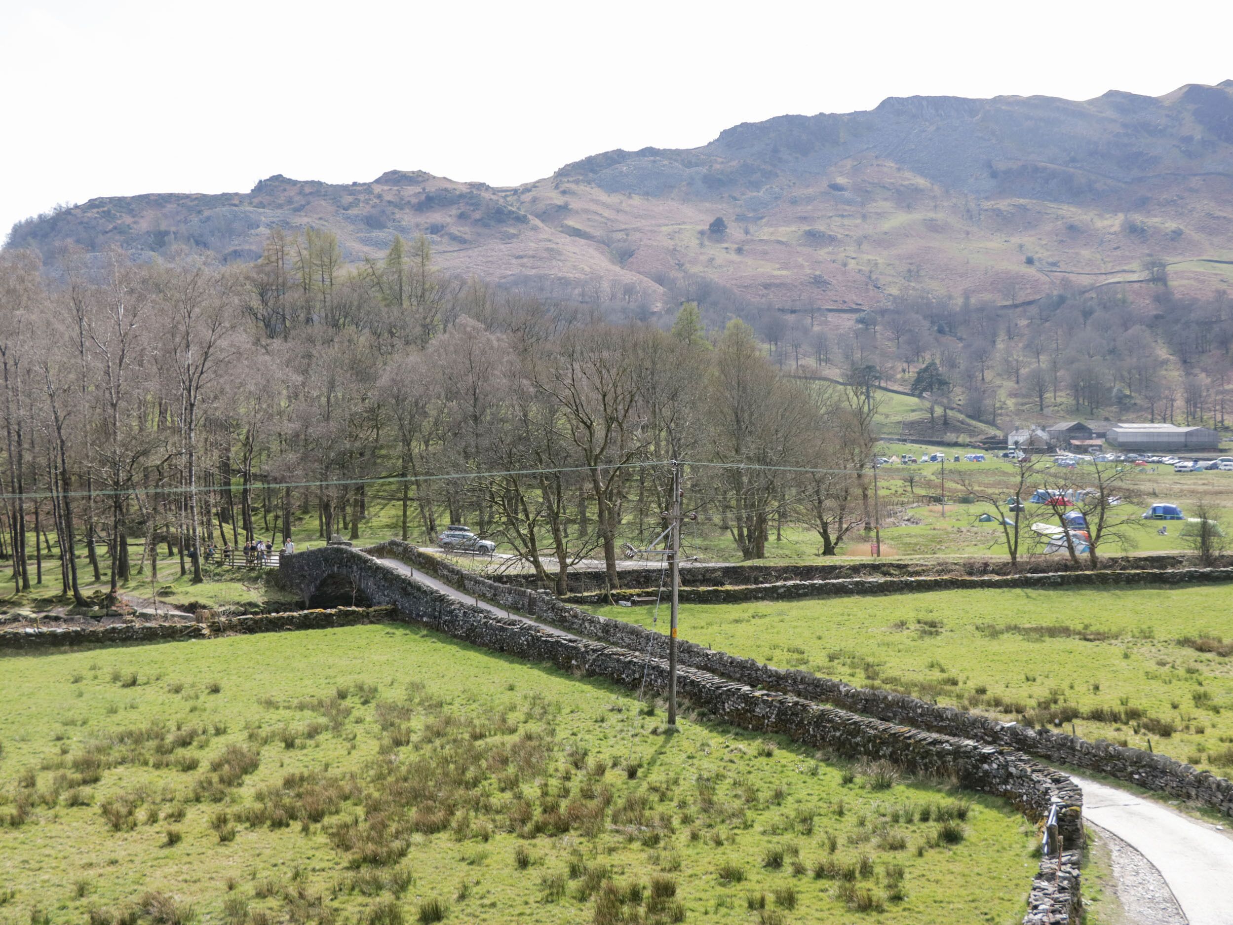 A rural landscape with a stone bridge, grassy fields, and a mountainous backdrop.