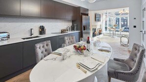 A modern kitchen with dark cabinets, a marble countertop, and a dining area with a round table set for six. - Host & Stay | Oxford House (Harrogate)
