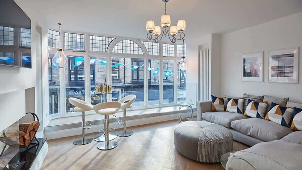 A modern living room with a large window, a chandelier, a sofa set, and a glass coffee table. - Host & Stay | Oxford House (Harrogate)