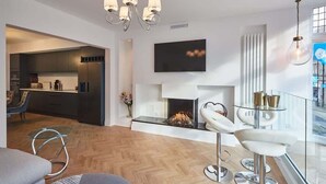 A modern living room with a fireplace, a dining area with a glass table, and a kitchen in the background. - Host & Stay | Oxford House (Harrogate)