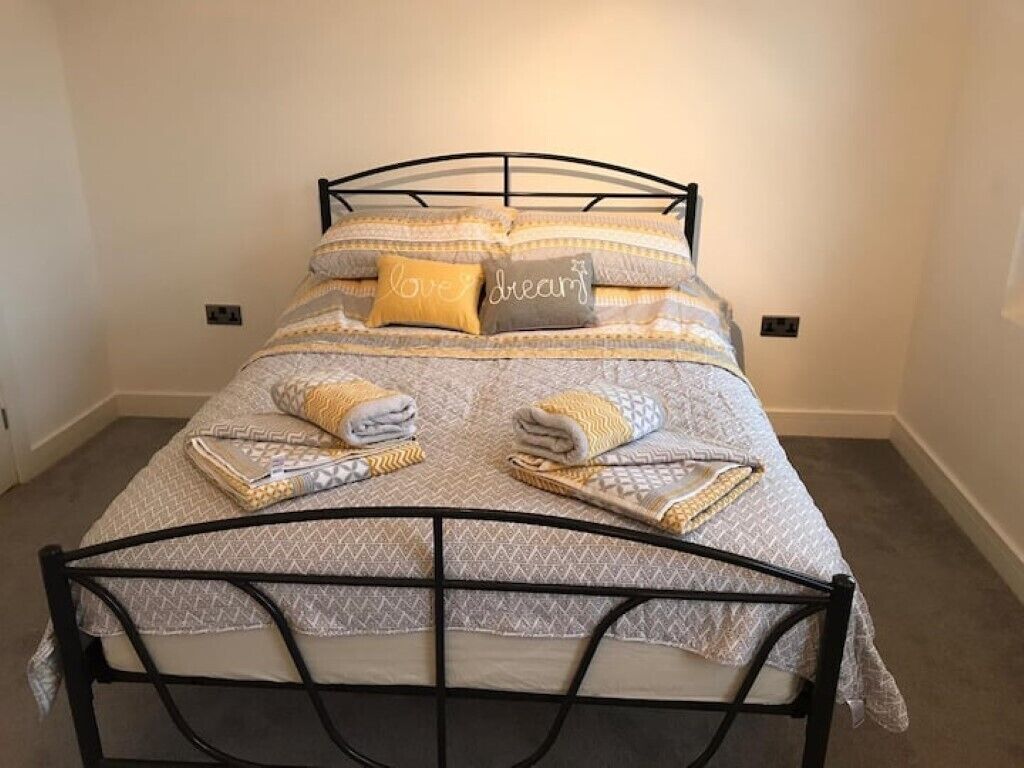A neatly made bed with patterned bedding and pillows, a metal headboard, and a folded towel on the bed.