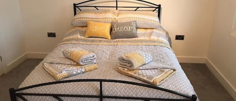 A neatly made bed with patterned bedding and pillows, a metal headboard, and a folded towel on the bed.
