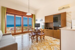 Enjoy a sea view from the large window in this living room, featuring a dining table, sofa, and TV.