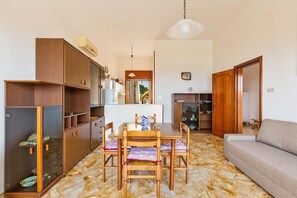 A compact living space with a dining table, wooden chairs, a sofa, and built-in wooden cabinets.