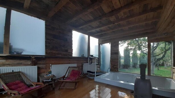 A log cabin interior with a wooden floor, a large window, a fireplace, and a hot tub. - Apartment Dujmović 1 (Otocac)