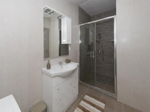 A modern bathroom with a white sink, a mirror, a cabinet, and a glass shower enclosure. - Apartment Dujmović 1 (Otocac)