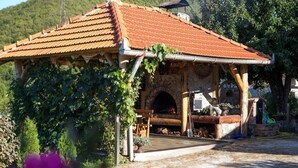 A rustic outdoor structure with a tiled roof, a stone fireplace, and a wooden bench. - Apartment Dujmović 1 (Otocac)