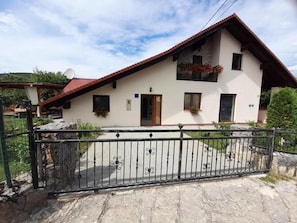 A two-story house with a red-tiled roof, a balcony with flowers, and a stone fence. - Apartment Dujmović 1 (Otocac)