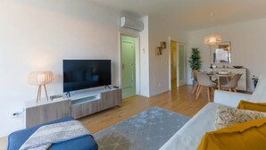 Un soggiorno moderno con una TV a schermo piatto, un'area pranzo con tavolo e sedie, e un angolo cottura con un tavolo da pranzo e sedie.
