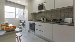 Una cucina moderna con mobili bianchi, un forno a microonde, un tostapane e un lavandino. Sul bancone c'è una ciotola di frutta e, nell'angolo, una lavatrice.