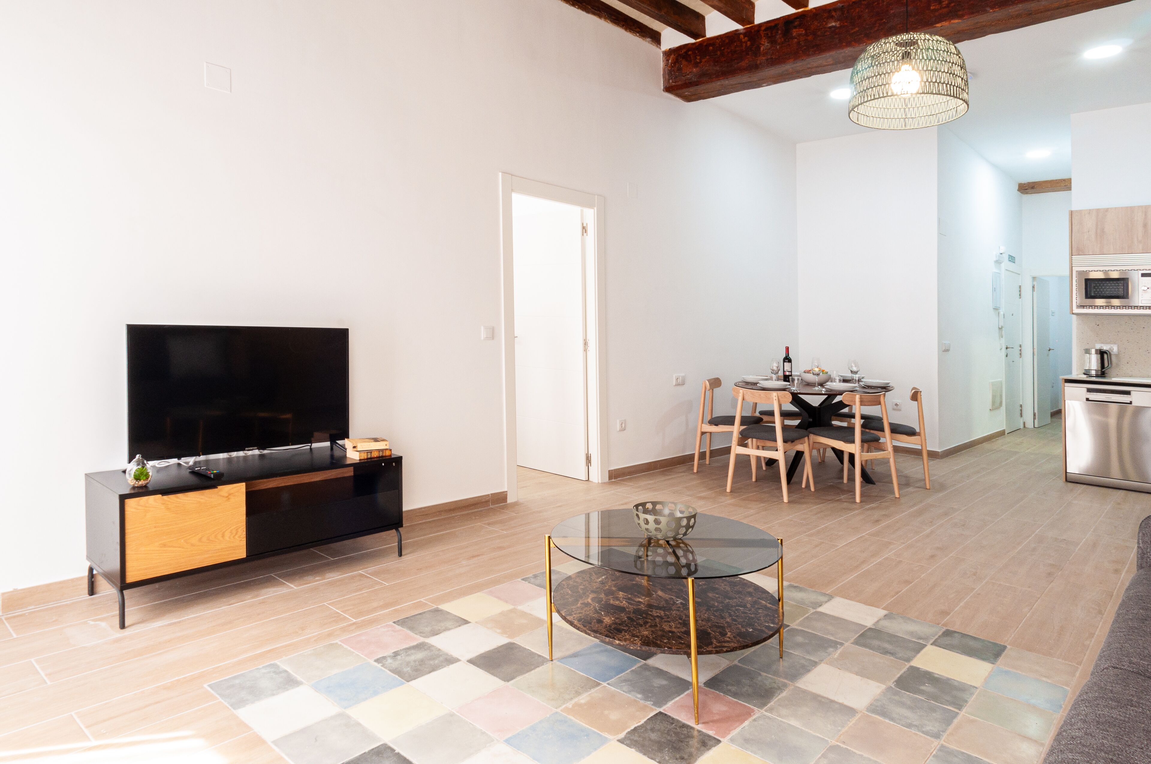A modern living room with a flat-screen TV, a glass coffee table, and a dining area with a wooden table and chairs.