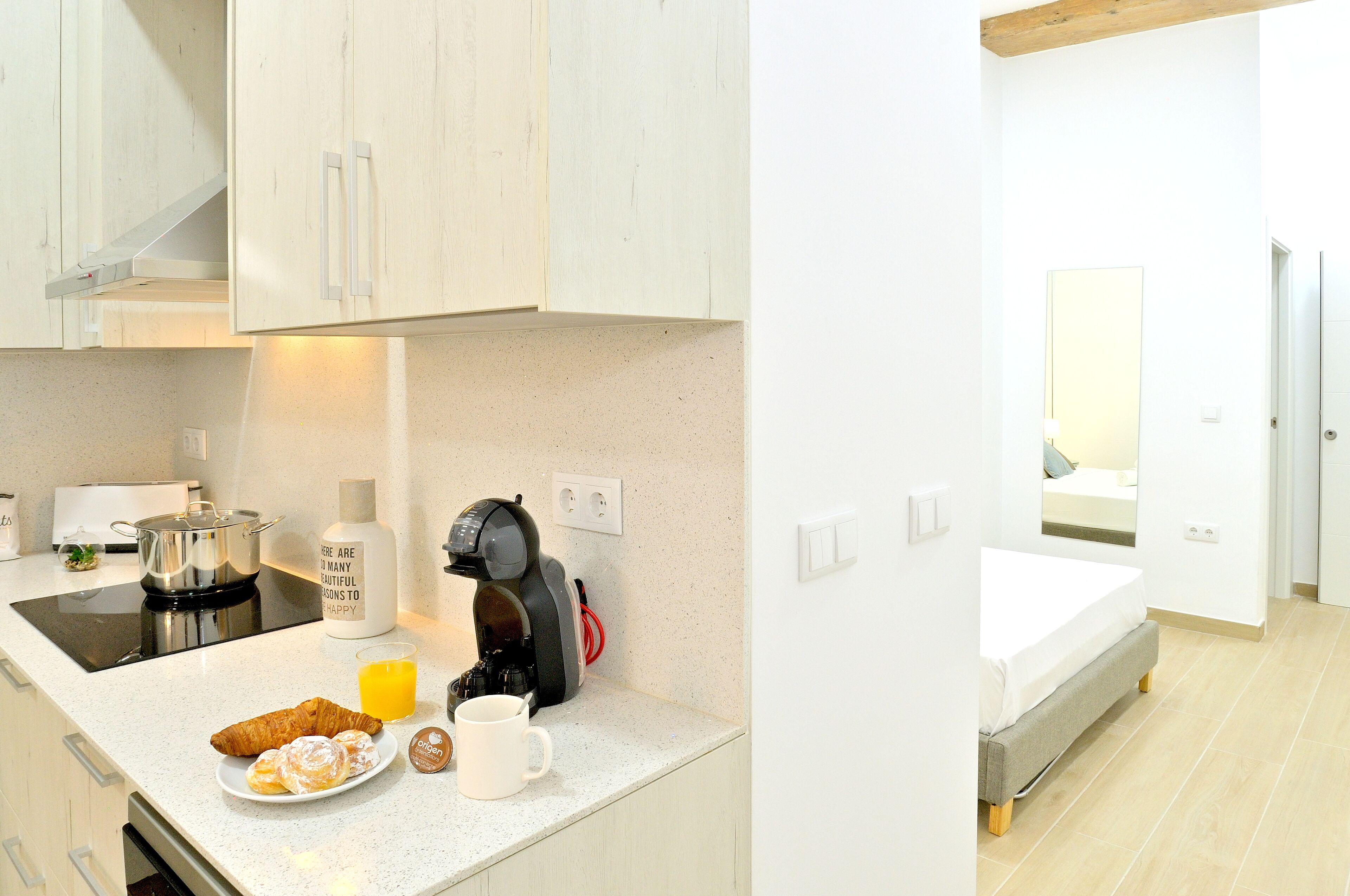 A modern kitchen with a coffee machine, a plate of croissants, and a glass of orange juice.