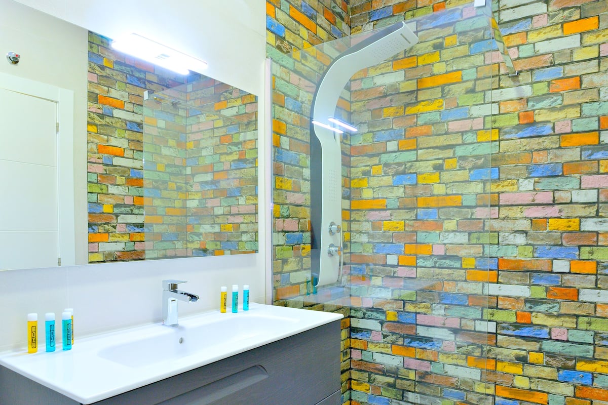 A bathroom with a white sink, a mirror, and a shower with a colorful brick wall.