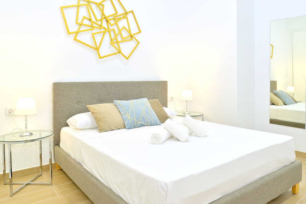 A neatly made bed with pillows, a bedside table with a lamp, and a wall-mounted geometric decoration.