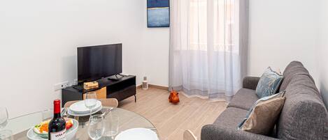 A modern living room with a round glass table, a sofa, a television, and a painting on the wall.
