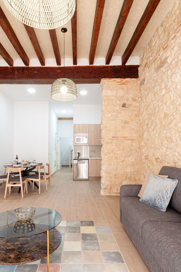 A modern kitchen with a stone wall, a dining area with a glass table, and a gray sofa with patterned cushions. - Myflats Luxury Bailen (Alicante)