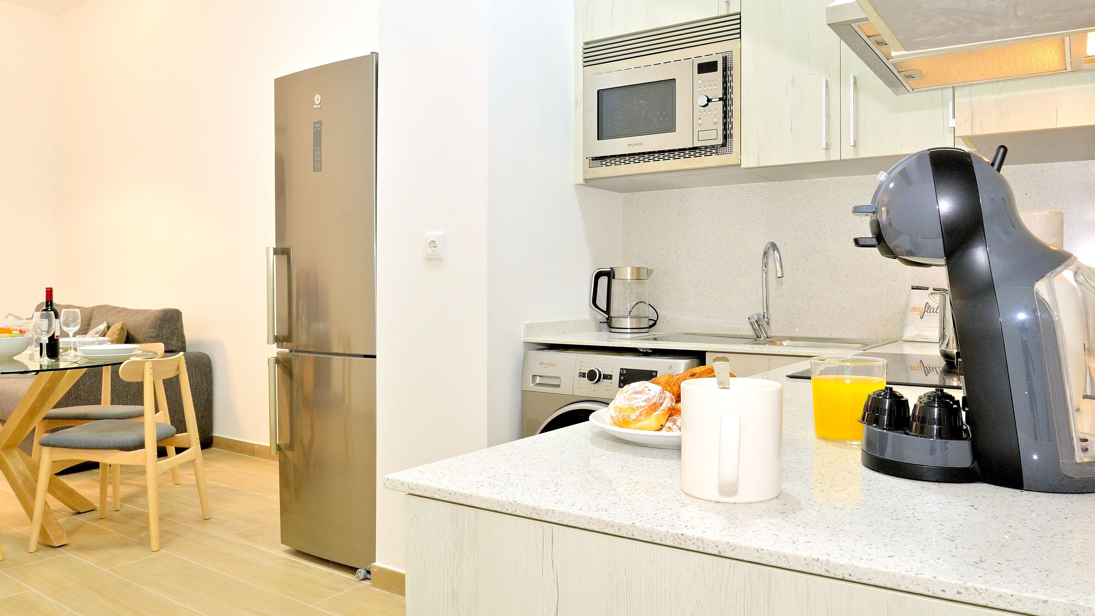 A compact kitchen with a refrigerator, microwave, coffee maker, and a blender on the counter.