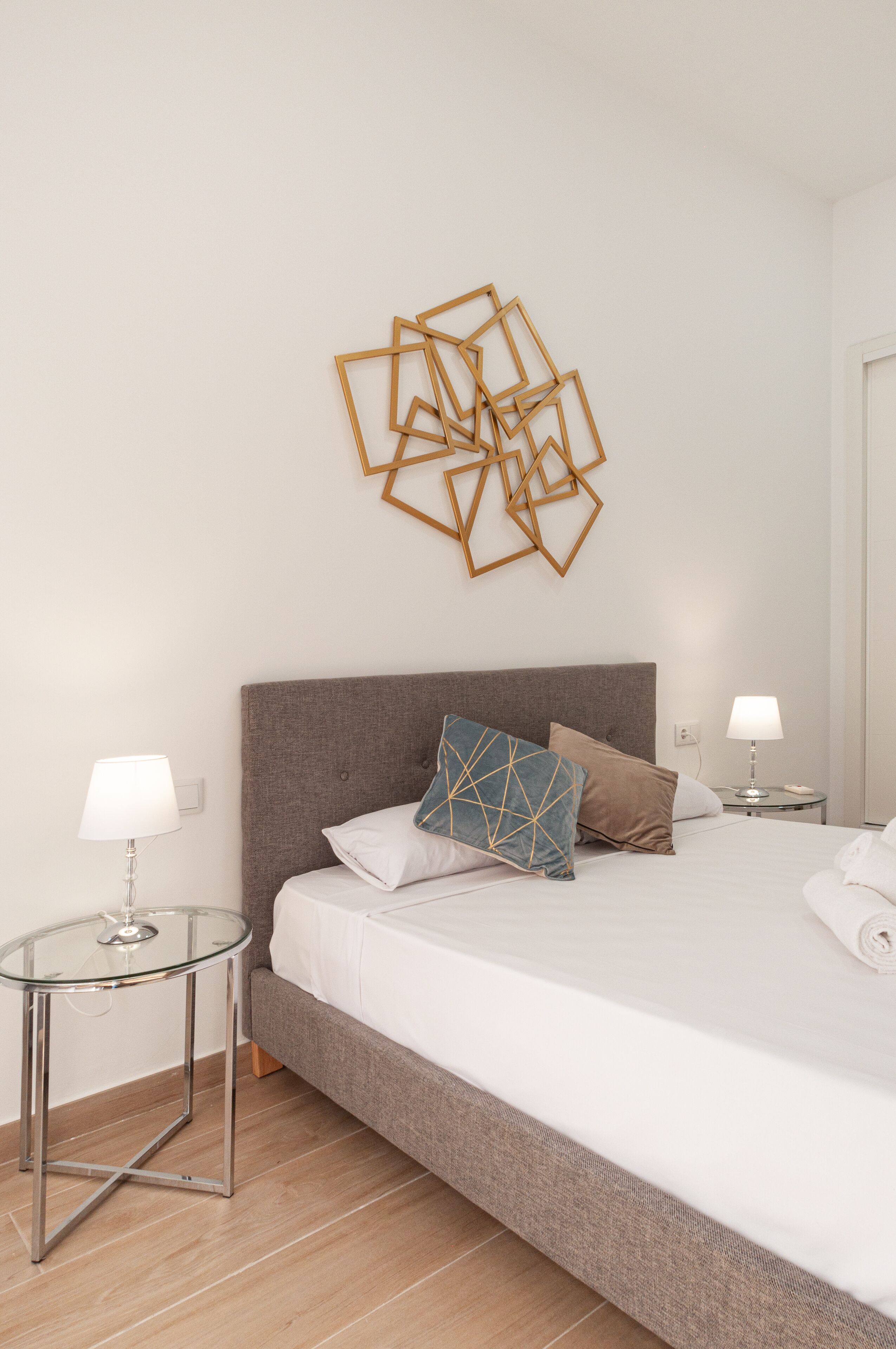 Un dormitorio ordenado con una cama grande, dos mesitas de noche y un adorno geométrico en la pared.