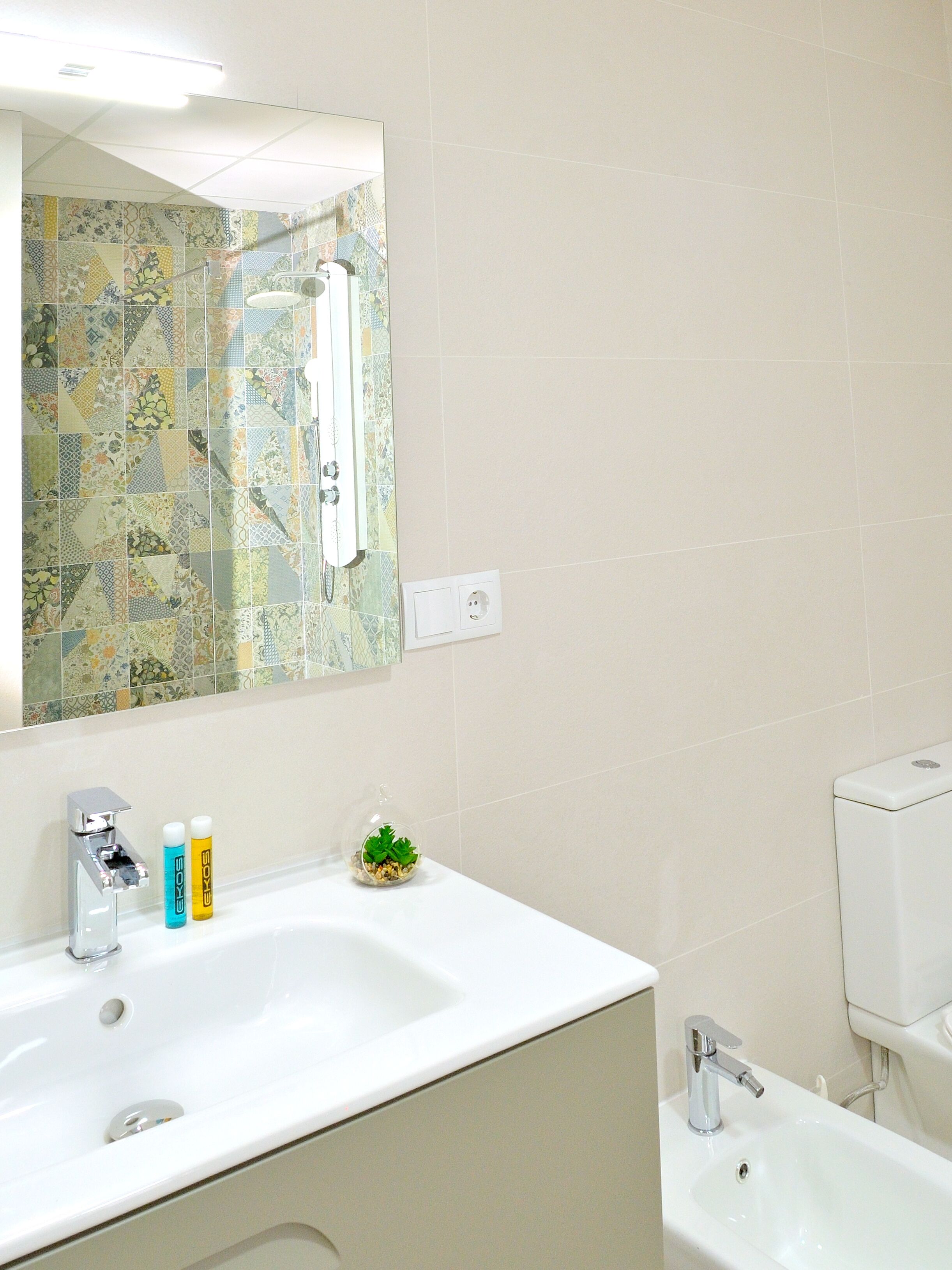 Une salle de bain avec un lavabo blanc, un miroir, une douche et des toilettes.