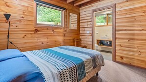 A wooden-paneled bedroom with a bed, a window, and a bathroom visible through an open door. - Stunning holiday home that has you feeling like you are in a Swiss chalet (Blairgowrie)